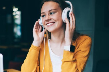 Neşeli hippi kız multimedya uygulaması ve kulaklıkla olumlu müzik listesi dinliyor, mutlu gülümseyen kadın kulaklıkla yüksek sesli favori müziğin tadını çıkarıyor ve dizüstü bilgisayarla ön tarafta oturuyor.