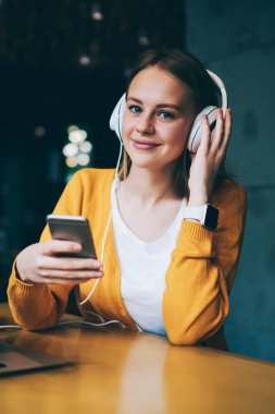 Elektronik kulaklıklı pozitif kadın melodinin portresi ilginç ses kitapları dinliyor ve sosyal ağlardaki arkadaşlarla mesajlaşıyor kafeteryadaki akıllı telefondan 4 g bedava internet kullanıyor.