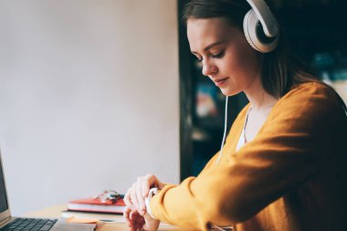 Genç bir kadın, kulaklıkla ciddi ses kitaplarını dinlerken GPS takibini ve takılabilir akıllı saatleri kontrol ediyor. Kafeteryada dizüstü bilgisayarla oturan, kulaklıklı, beyaz bir hippi kız.