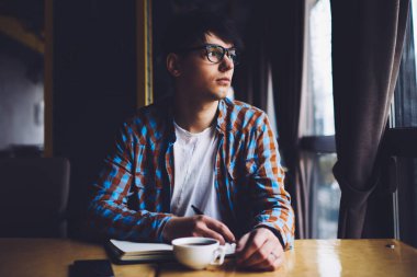 Gözlüklü düşünceli genç adam pencereden dışarı bakıyor ve elinde kalemle masada oturan yeni bir roman yazmayı düşünüyor. Gözlüklü bir öğrenci kahve dükkanında ödev yapıyor.