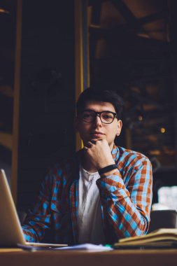 Optik gözlüklü zeki öğrencilerin portresi kameraya bakıyor kitaplara bakıyor ve hızlı internet bağlantısı olan modern bilgisayarlara bakıyor. Kafenin içinde serbest çalışan erkek metin yazarı.