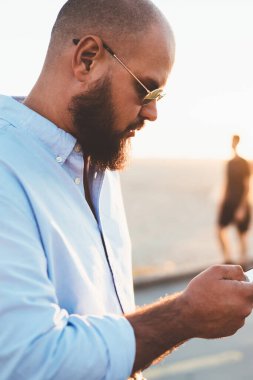 Dalgın sakallı adam akıllı telefon hücresel açık havada duran üzerinden sosyal ağlar bloglama içerik yükleme sokak, erkek hipster üzerinde iyi bir internet bağlantısı üzerinden uygulama yükleme