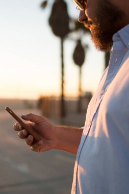 Hipster adam modern cep telefonu elinde göz web sayfasından, genç adam 4 g internet bağlantısı açık havada duran kullanarak Smartphone'da kısa mesaj gönderme haber okuma görünümünü kırpılmış