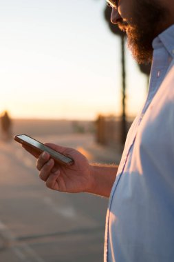 Genç adam online şehir sokak, hipster adam pay fotoğraf blog yolu ile uygulama açık havada süre sosyal ağlar posta kontrol üzerinde ayakta rezervasyon yapmak için smartphone kullanarak görünümünü kırpılmış