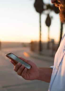 Sakallı erkek holding cep telefonu haber bilgi göz web sayfası ayakta Caddesi üzerinde okuma, Resim kırpılmış, hipster adam görüş fotoğraf içinde sosyal ağlar bloglama online yolu ile smartphone