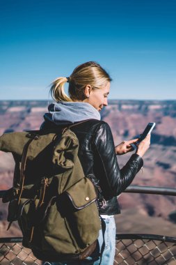 Dağlarda, pozitif kadın Gezgin vahşi doğa keşfetmek akıllı ileti gönderme turistik güzergah üzerinde hiking iyi mobil bağlantı kontrol sırt çantası ile genç hippi kız avare gülümseyen