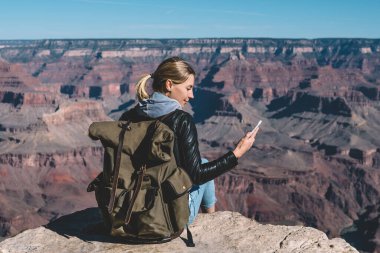 Dağın tepesinde Büyük Kanyon Milli Parkı'nda, hippi kız mesaj göndermek için iyi şebeke kapsama alanı ile yürüyüş zevk oturan mobil veri bağlantı denetimi smartphone tutan kadın Gezgin