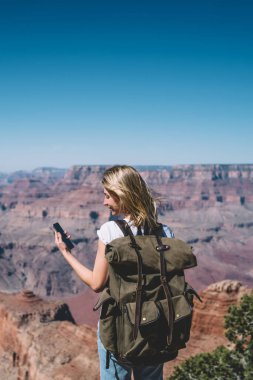 Genç hippi kız okuma mesajı smartphone ayakta dağlar bakış açısı gezici, kadın turist tur sırasında iletişim kurmak için doğada iyi mobil veri bağlantısı kullanarak sırt çantası ile kullanma