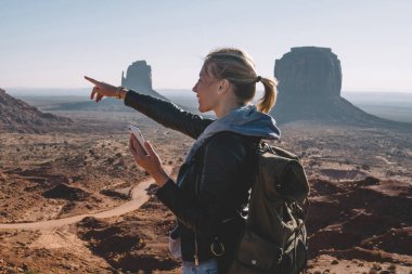 Hippi kız manzara doğa görünümü ortamında smartphone, kadın Gezgin Monument Valley hedefe getting zevk telefonu uygulaması kullanarak tutan Navajo rezervasyon işaret gülümseyen
