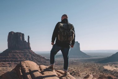 Monument Valley, vahşi çevre keşfetmek hedefe getting erkek yolcu Yolculuk tutkusu kuru çöl toprakları yüksek güzel sahne görünümünde bakarak kayada duran sırt çantası ile arkadan görünüşü adam