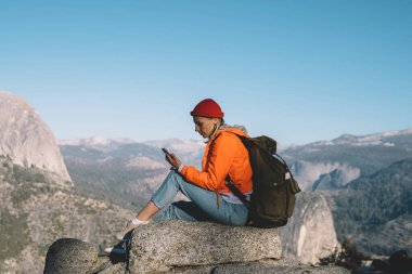 Yürüyüş turu sırasında yüksek kayalıklarda dinlenen genç bir kadın mesaj yolluyor. Kadın gezgin, vahşi doğayı keşfederken telefon yoluyla posta göndermek için iyi bir cep telefonu bağlantısına sahip.