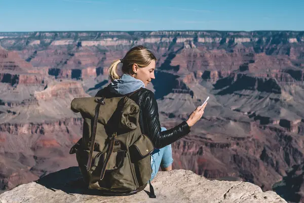 Dağın tepesinde Büyük Kanyon Milli Parkı'nda, hippi kız mesaj göndermek için iyi şebeke kapsama alanı ile yürüyüş zevk oturan mobil veri bağlantı denetimi smartphone tutan kadın Gezgin