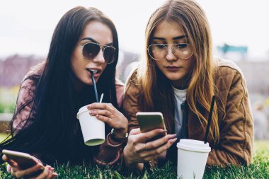 Central Park'ta çim üzerinde yalan ve sosyal ağlar üzerinde akıllı telefonlar kolay sohbet mesajlaşma süre alanını sahte ile lezzetli kahve içecek içme şık Güneş gözlükleri çekici genç kadın