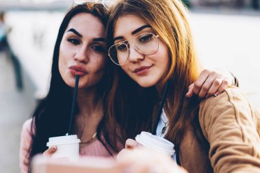 Görüntü lezzetli kahve ön kamera dijital hareket eden telefon aygıt üzerinde seyir ve kentsel ortamda dostu toplantı sırasında fotoğraf çekmek elinde olan çekici gülümseyen genç kadın kapatmak