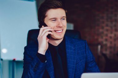 Gülümseyen erkek yönetici müşteri hizmetlerine hesap bakiyesini kontrol etmeleri için sesleniyor. Haberlerden heyecanlanan başarılı iş adamı telefon görüşmeleri sırasında netbook ile ahşap masada oturuyor.