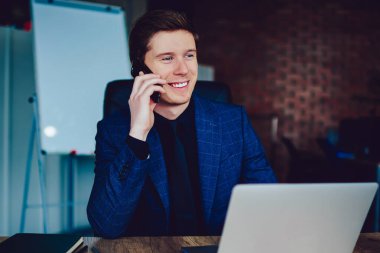 Gülümseyen erkek yönetici müşteri hizmetlerine hesap bakiyesini kontrol etmeleri için sesleniyor. Haberlerden heyecanlanan başarılı iş adamı telefon görüşmeleri sırasında netbook ile ahşap masada oturuyor.