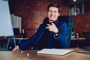 Masaüstünde oturan başarılı erkek yönetmenin portresi kameraya bakıyor ve neşeli ruh halinin keyfini çıkarıyor, resmi olarak pozitif iş adamı şirket ofisinde heyecanlı ve mutlu hissederek zaman geçiriyor.