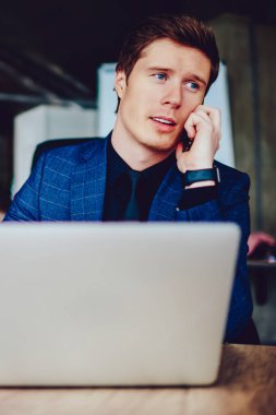 Kafkasyalı ciddi girişimci proje için yatırımcıyla önemli bir akıllı telefon görüşmesi yapıyor. Konsantre olmuş erkek patron elinde netbook ile masaüstünde oturuyor ve danışmanlık için operatöre telefon ediyor.