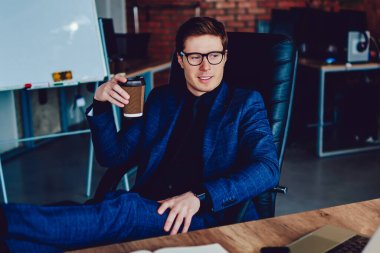 Pozitif erkek girişimci kahve molası veriyor ve ofiste çalıştıktan sonra dizüstü bilgisayarla komik filmler izliyor başarılı iş adamı elinde kafein içeceği tutuyor ve Webinar 'dan mutlu oluyor.