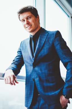 Pencerenin yanında durup kameraya bakan başarılı beyaz erkek portresi, şirket ofisinde boş zamanlarında poz veren pozitif gülümseyen iş adamı, liderlik ve istihdam kavramı