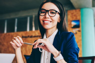 Kafkasyalı neşeli iş kadınının yarım boy portresi elinde kalem, yüzünde sevimli bir gülümsemeyle kameraya bakıyor, başarılı genç bayan iş arkadaşı şirket ofisinde yönetimden keyif alıyor.
