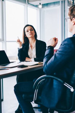 Kendine güvenen erkek yönetmen, genç internet reklamları, iş ve takım çalışması kavramları için ekran oluşturarak dizüstü bilgisayarın önünde oturan meslektaşlarına çalışma sürecini anlatıyor.