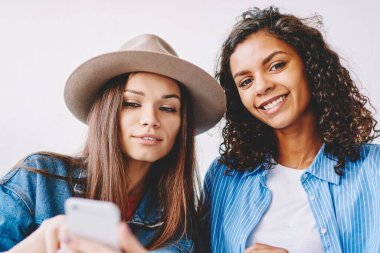 İki mutlu çok kültürlü bayan arkadaş birlikte vakit geçirip içeride eğleniyorlar. Modayı takip eden hippi kız modern akıllı telefon cihazından, yanında oturan kadına bilgi aktarıyor.