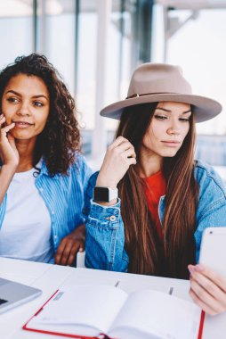 Güzel hippi kızlar, gelecekteki tatilleri planlamak için teknolojiyi kullanarak sokak kafeteryasında birlikte vakit geçiriyorlar. Çekici kadınlar, akıllı telefon cihazıyla ön kamerayla selfie çekiyorlar.