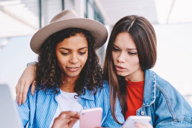 Akıllı telefon cihazları hakkında bilgi paylaşan çekici kadınlar dizüstü bilgisayarla aynı masada oturuyorlar iyi kablosuz bağlantı kullanıyorlar, çok kültürlü hipster kızları cep telefonuyla takipçilerle mesajlaşıyorlar.