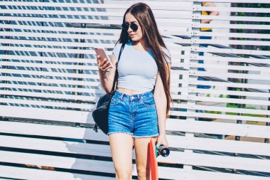 Hippi kız kaykay metin reklam için promosyon arka plan üzerinde ayakta açık havada süre elinde tutan smartphone cep telefonu ile ağdan gelen bildirim okuma rahat kıyafet giymiş