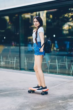 Kentsel ortamda kameraya gülümseyen sırasında kaykay sırt çantası ile güzel genç kadın portresi. Sportif hobi serbest zaman harcama on board sürme rahat yaz kıyafeti çekici patenci