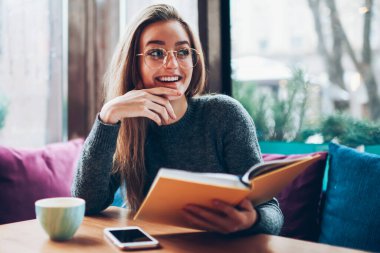 Moda kıyafetleri içinde genç, neşeli bir hippi kız elinde defterle kafeteryada arkadaşını bekliyor, gözde gözlükleriyle gülümseyen ve en sevdiği edebiyattan keyif alan bir kadın.