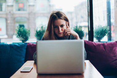 Kafeteryada dizüstü bilgisayarla otururken iş yerindeki görevler hakkında endişelenen genç, ciddi kadın yazarlar, konsantre hipster kız çevrimiçi kurs yoluyla programlamayı öğreniyor.