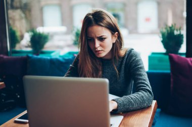 Aşırı çalışan kadın, kafeteryada oturmuş modern netbook 'u kullanarak ciddi şekilde internetten Webinar izliyor. Önemli bir proje için endişeleniyor. Mutsuz bir kız öğrenci bilgisayarla ev ödevlerini yapıyor.