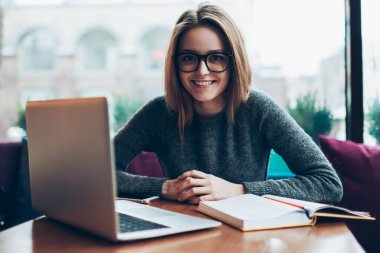 Sırıtkan profesyonel serbest çalışan bir kadının portresi dizüstü bilgisayarla ortak çalışma alanında oturuyor ve kameraya bakıyor, netbook üzerinden öğrenen neşeli hippi kız kampüste ödev yapıyor.