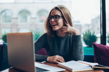 Genç mutlu bayan metin yazarı, yeni modern dizüstü bilgisayarla kafeteryada otururken yüzünde olumlu bir gülümsemeyle ev ödevini tamamlamaktan memnun kalmış tasasız bir öğrenci.