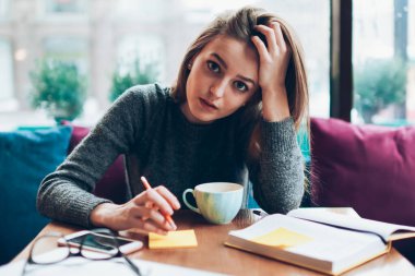 Üniversite kafeteryasında planlama için not defteriyle oturan genç ve ciddi bir kız öğrencinin portresi. Çekici hippi kız kameraya bakıyor ve ödev hazırlıyor. Çıkartmalarla notlar alıyor.