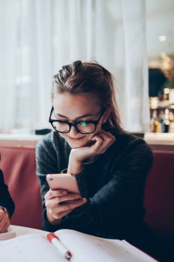 Moda gözlüklü yakışıklı hippi bir adamın portresi kameraya bakarken bir yandan da cep telefonuyla sohbet eden bir kadının yanında çalışıyor. Yüzünde sevimli bir gülümseme var.