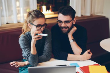 İki mutlu meslektaşın görüş koruması için gözlük. Dizüstü bilgisayar ve başlangıç projesinde çalışmaktan keyif alıyorlar. Birkaç gülümseyen hipster blogcu içeride birlikte vakit geçiriyorlar.