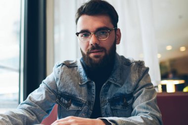 Üniversite kafe 'sinde oturan yakışıklı, ciddi bir erkek yazarın portresi. Çalışırken kameraya bakıyor. Kot giyimli modaya uygun hippi adam ve görüş düzeltici gözlük takıyor.