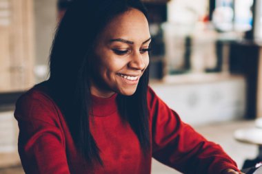 Koyu tenli kız öğrenci kafede oturan e-posta iletisini mutlu gülümseyerek. Başarılı afro Amerikan blogger takipçileri ile sohbet ve paylaşım bilgi ve multimedya cep üzerinde