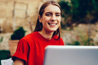 Dizüstü bilgisayarla çalışan neşeli kadın metin yazarının portresi ve açık havada gülümseyen kameraya bakmak, üniversite kampüsünde netbook üzerinden dil öğrenen neşeli hippi kız.