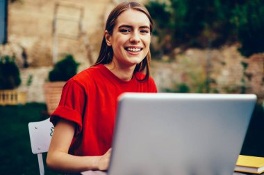 Dizüstü bilgisayarla çalışan neşeli kadın metin yazarının portresi ve açık havada gülümseyen kameraya bakmak, üniversite kampüsünde netbook üzerinden dil öğrenen neşeli hippi kız.