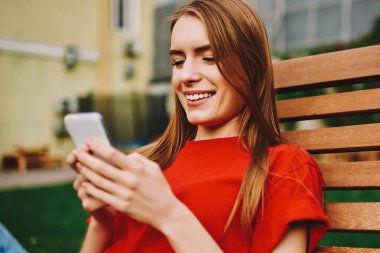 Neşeli hippi kız mesajlar yazıyor ve kampüste bankta dinlenirken akıllı telefondaki uyarıları kontrol ediyor, cep telefonu kullanan mutlu kadın 4G internetli ve açık havada blog yazıyor.