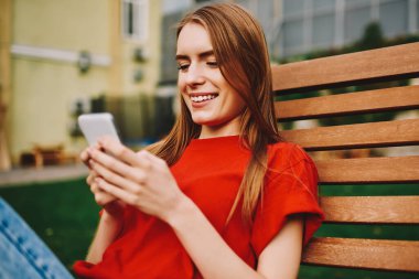 Neşeli hippi kız mesajlar yazıyor ve kampüste bankta dinlenirken akıllı telefondaki uyarıları kontrol ediyor, cep telefonu kullanan mutlu kadın 4G internetli ve açık havada blog yazıyor.