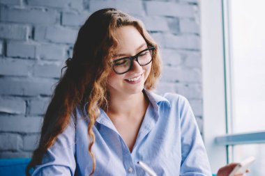 Sosyal ağlarda eğlenceli videolar izleyen pozitif kız öğrenci tatil planlarken ve mobil uygulama üzerinden rezervasyon yaparken, internet sitesindeki arkadaşlarıyla mesajlaşan mutlu hippi kız