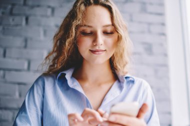 Sohbet etmek için mobil uygulama üzerinden SMS yazan, modern akıllı telefon cihazını güncelleyen mutlu, gülümseyen bir kadın.