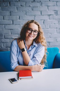 Moda gözlüklü mutlu hippi kızın portresi, kafeteryada otururken göz koruması sağlamak ve boş zamanlarında kameraya gülümsemek, en çok satan veya ders kitabı olarak masada kalmak.