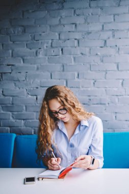 Kafeteryadaki mülakatlardan sonra not defterine bilgi yazan çekici genç bayan gazeteci, gözlüklü güzel kadın içeride arkadaşını beklerken ders kitabında ilginç düşünceleri not alıyor.