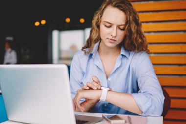 Ciddi kadın serbest çalışan, kafeteryada iş arkadaşıyla buluşmayı beklerken elektronik akıllı saati kontrol ediyor. Mesafeli çalışma alanında kol saati üzerinden GPS 'i takip eden genç bir kadın.